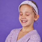 Young girl wearing a purple headband and sweater against a purple background