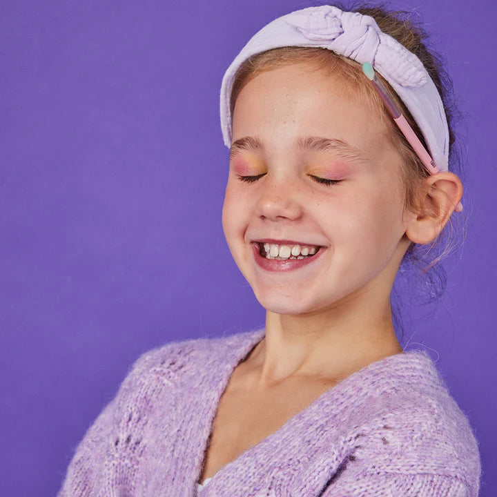 Young girl wearing a purple headband and sweater against a purple background