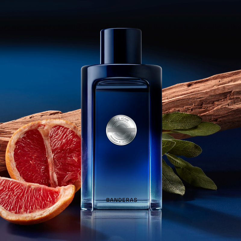 Blue Banderas perfume bottle with sliced grapefruit and cinnamon sticks on a dark background
