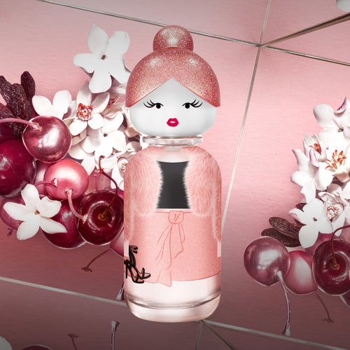 Pink perfume bottle with decorative top against a floral and cherry background