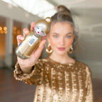 Woman holding a gold bottle with a decorative cap, blurred indoor background
