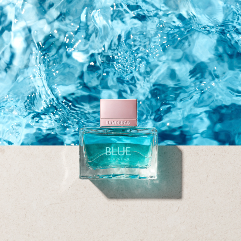 Blue perfume bottle with pink cap on a white surface with blue water in the background