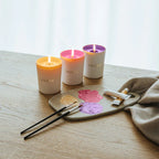 Three Lalique candles on a wooden table with a paint palette and brushes.