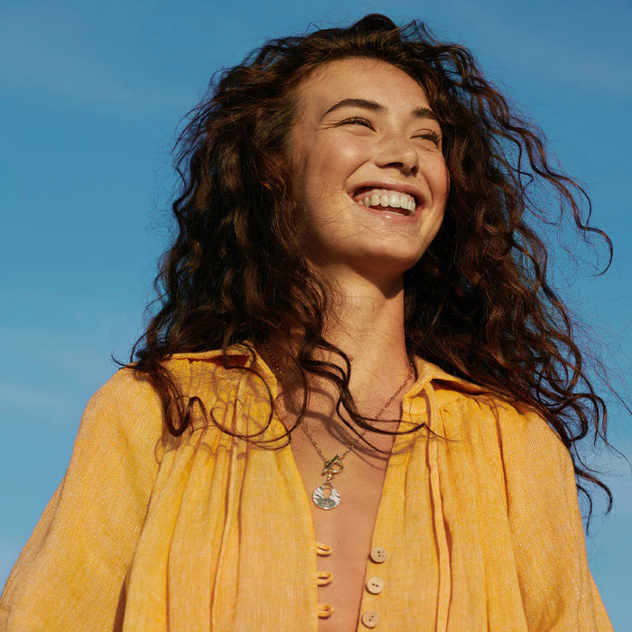 Woman with curly hair wearing a yellow shirt against a blue sky