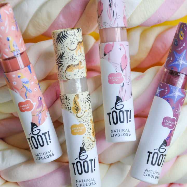 Collection of TOOT! lip gloss tubes with colorful designs on a floral background
