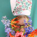 Person with colorful flowers around their head, wearing a 'TOOT!' cosmetic bag.